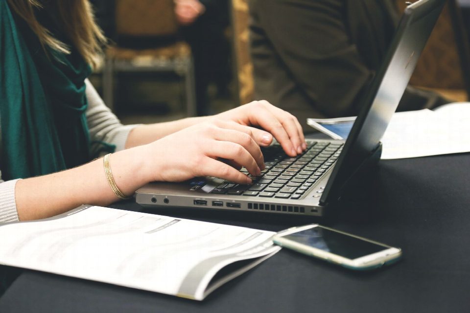Adult woman typing on a laptop at a desk with a smartphone and documents. Adult woman typing on a laptop at a desk with a smartphone and documents.